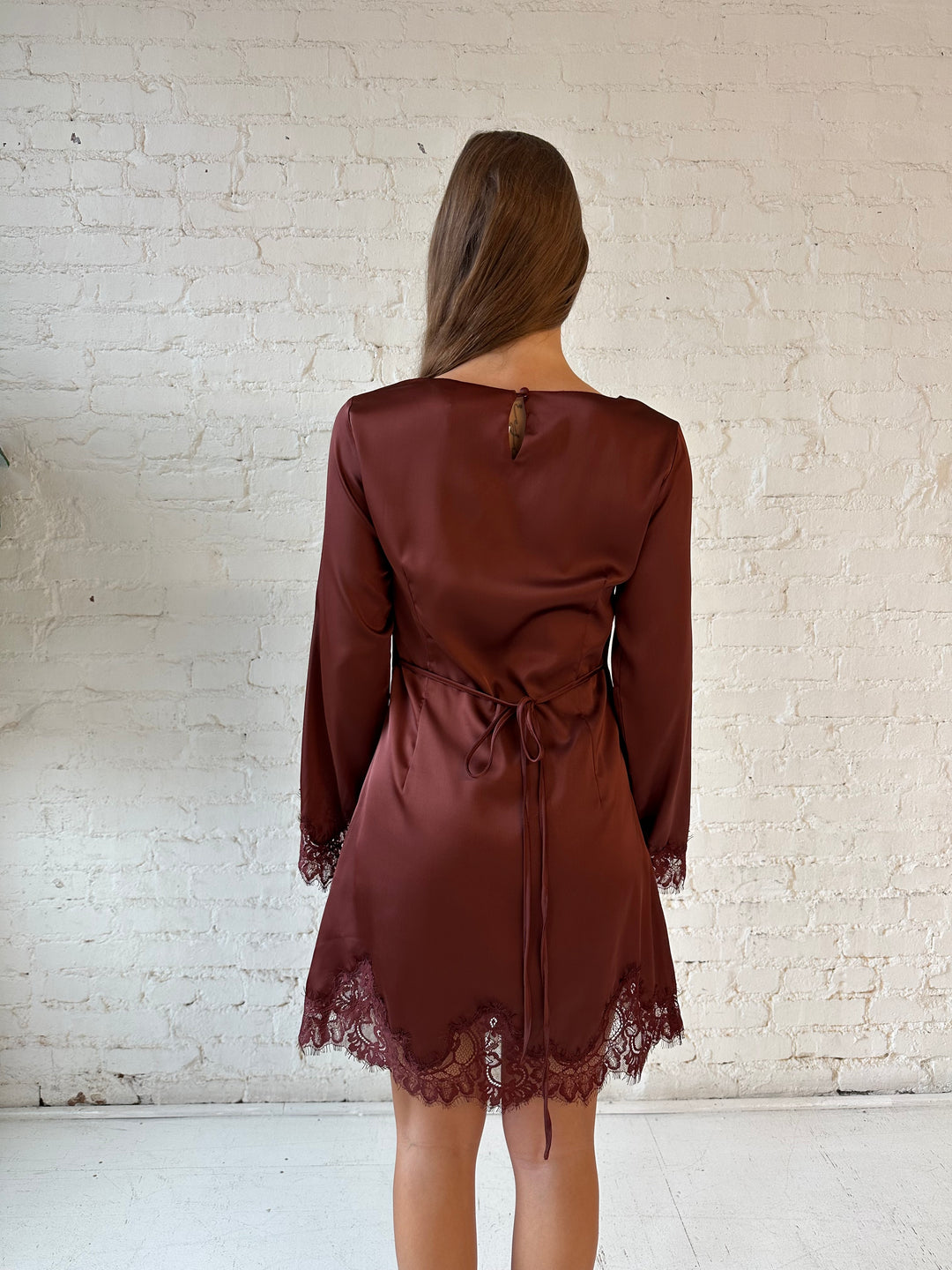 Woman wearing rust satin mini dress with long sleeves and lace trim detail.