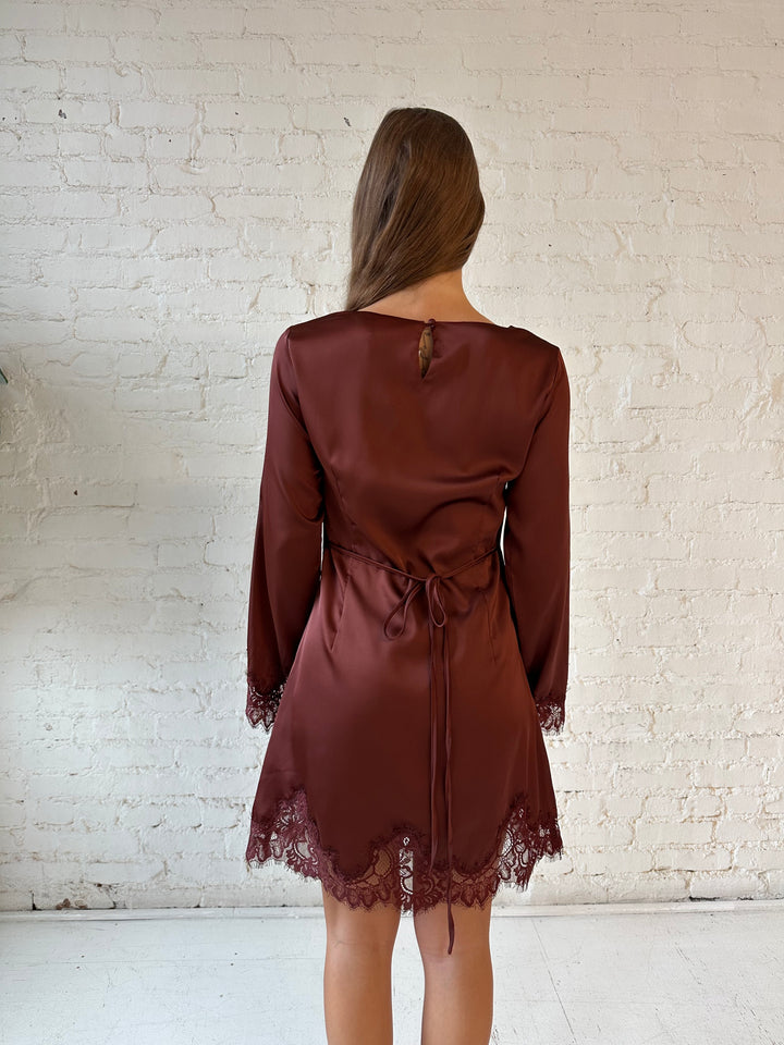 Woman wearing rust satin mini dress with long sleeves and lace trim detail.