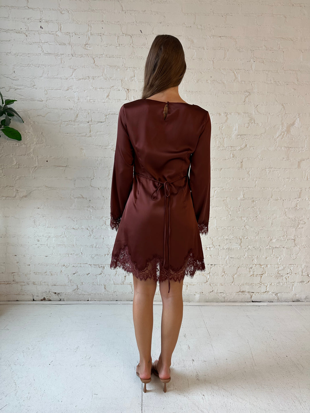 Woman wearing rust satin mini dress with long sleeves and lace trim detail.