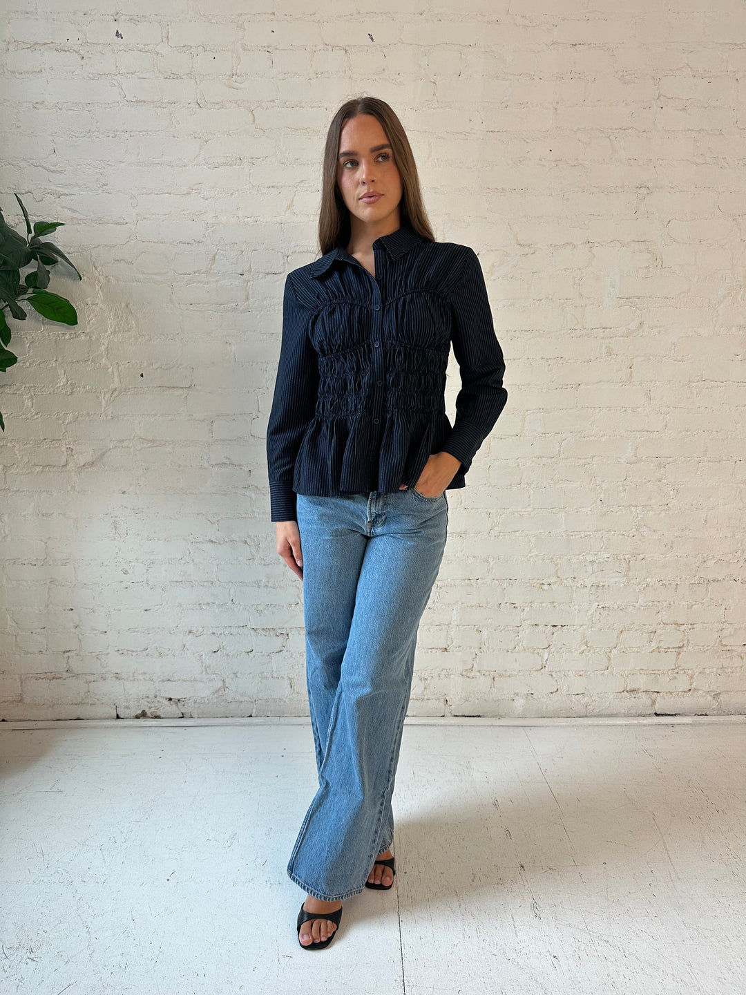 Woman wearing navy blue pinstripe long sleeve peplum top with medium wash jeans.