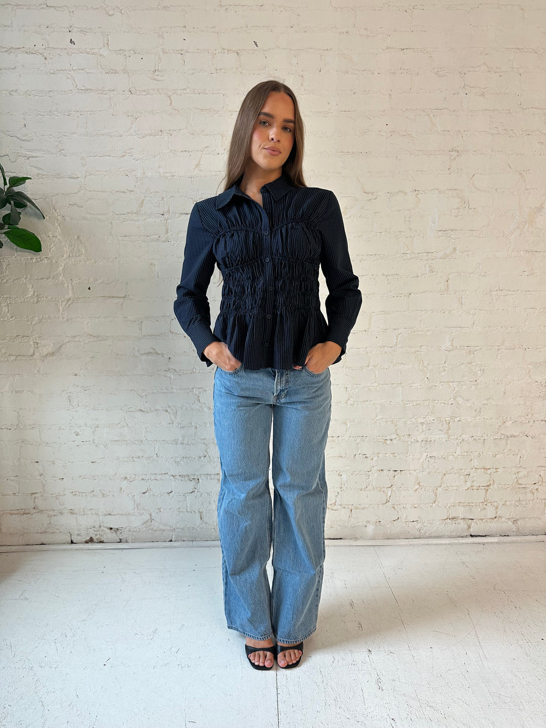 Woman wearing navy blue pinstripe long sleeve peplum top with medium wash jeans.