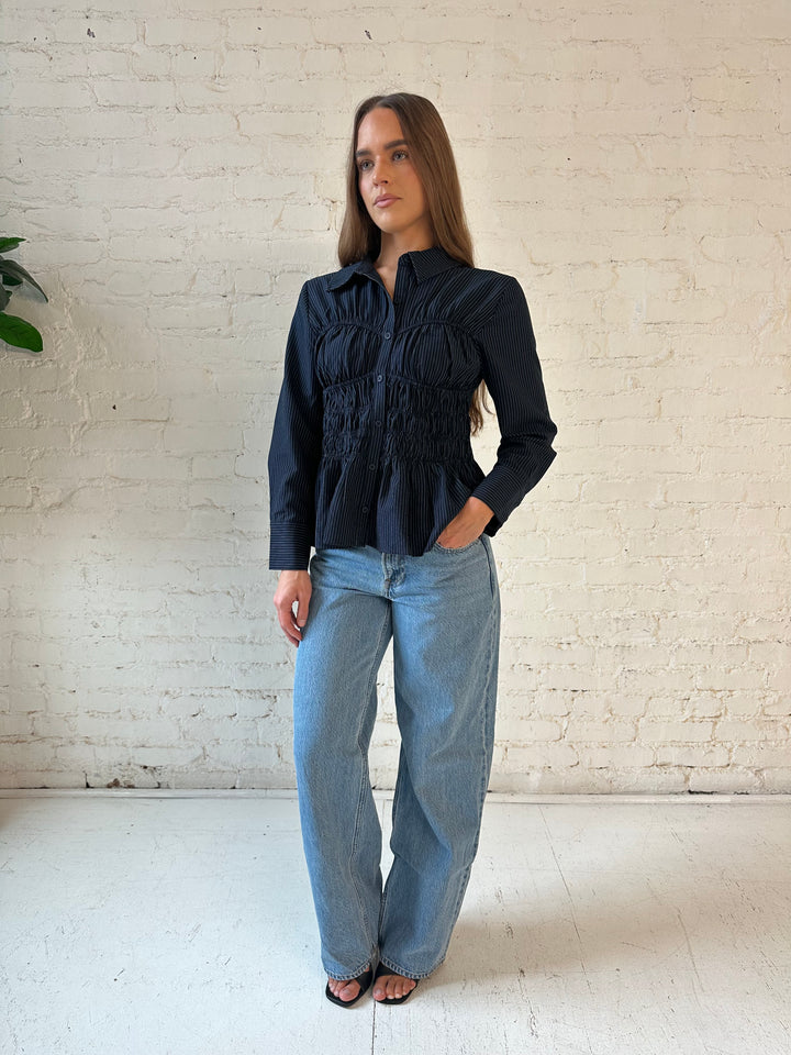 Woman wearing navy blue pinstripe long sleeve peplum top with medium wash jeans.