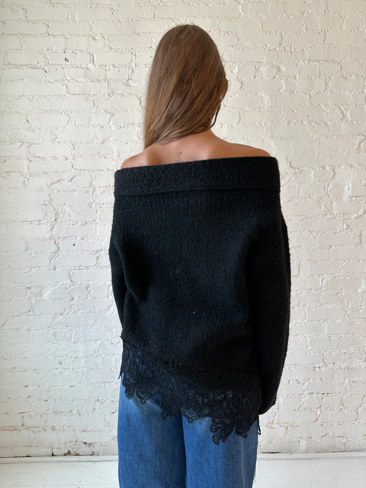 Woman wearing black knit, off the shoulder sweater with lace trim hem, and dark wash jean.