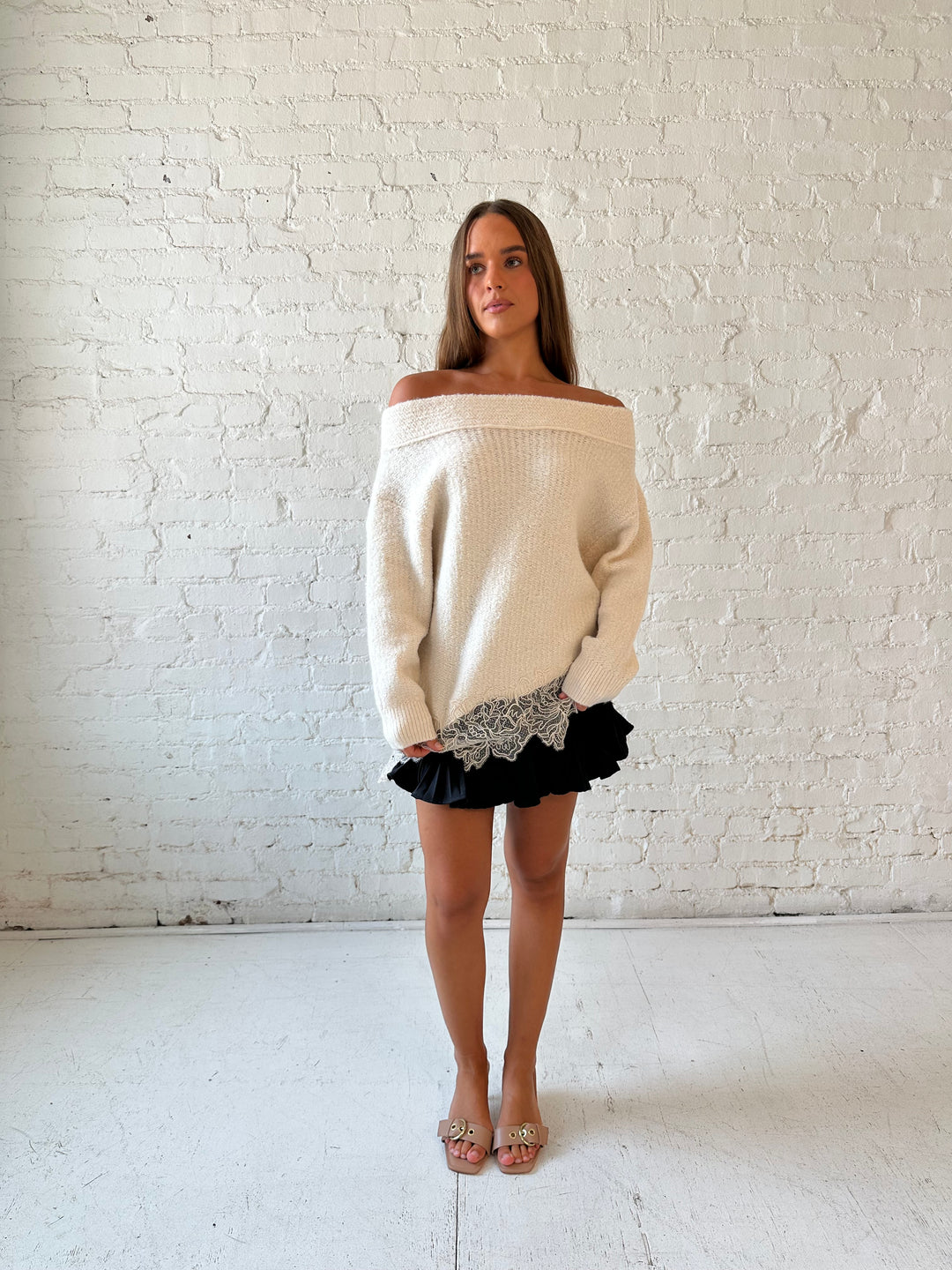 Woman wearing cream off the shoulder sweater with lace trim hem and charcoal pleated mini skort. 