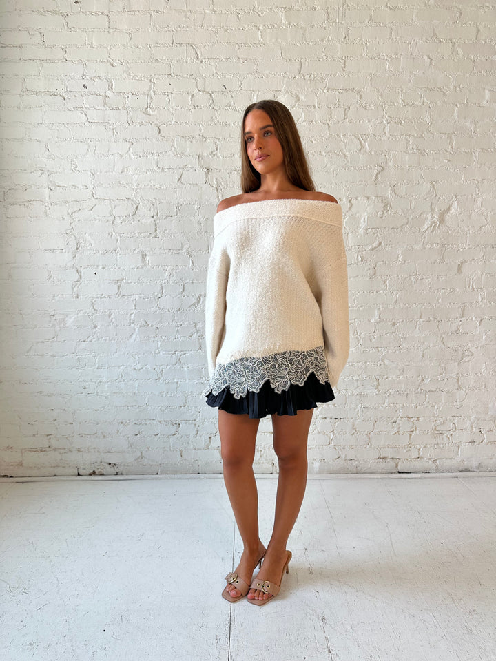 Woman wearing cream off the shoulder sweater with lace trim hem and charcoal pleated mini skort. 