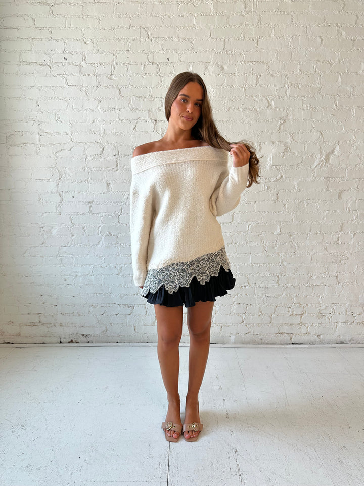 Woman wearing cream off the shoulder sweater with lace trim hem and charcoal pleated mini skort. 