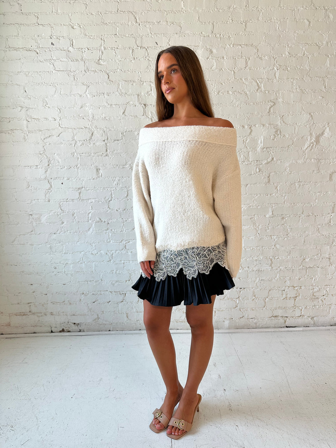 Woman wearing cream off the shoulder sweater with lace trim hem and charcoal pleated mini skort. 