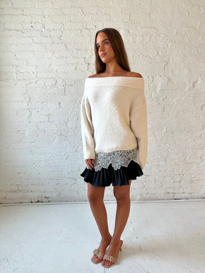 Woman wearing cream off the shoulder sweater with lace trim hem and charcoal pleated mini skort. 