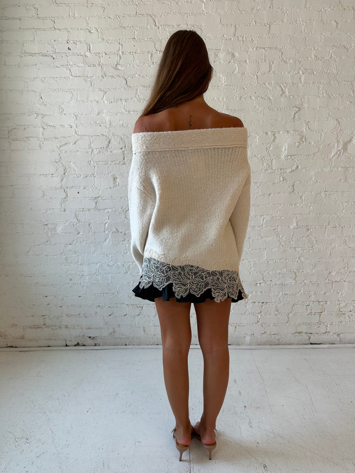 Woman wearing cream off the shoulder sweater with lace trim hem and charcoal pleated mini skort. 