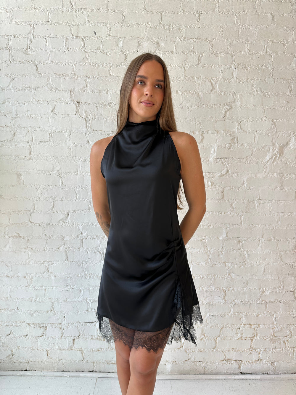 Woman wearing black satin mini dress with cowl halter neckline and lace trim detailing 
