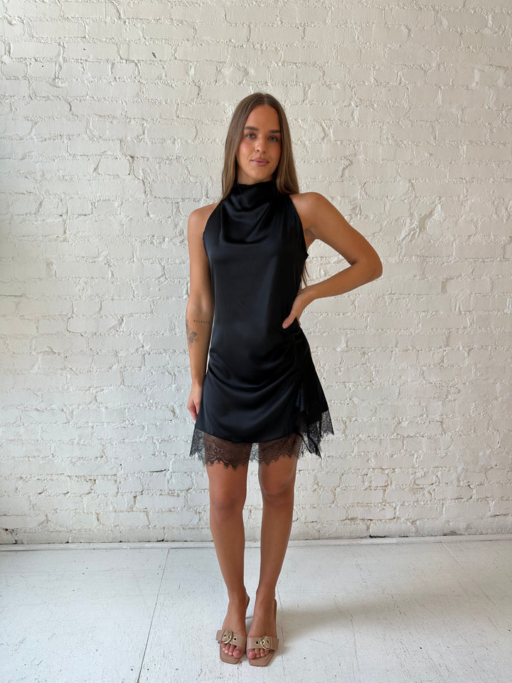 Woman wearing black satin mini dress with cowl halter neckline and lace trim detailing 