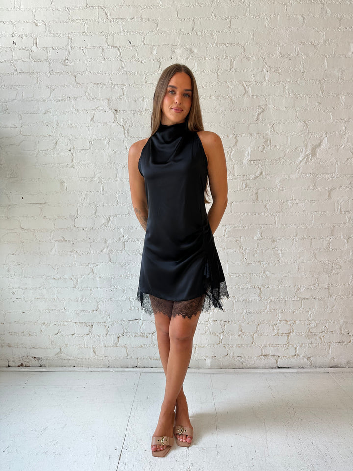 Woman wearing black satin mini dress with cowl halter neckline and lace trim detailing 