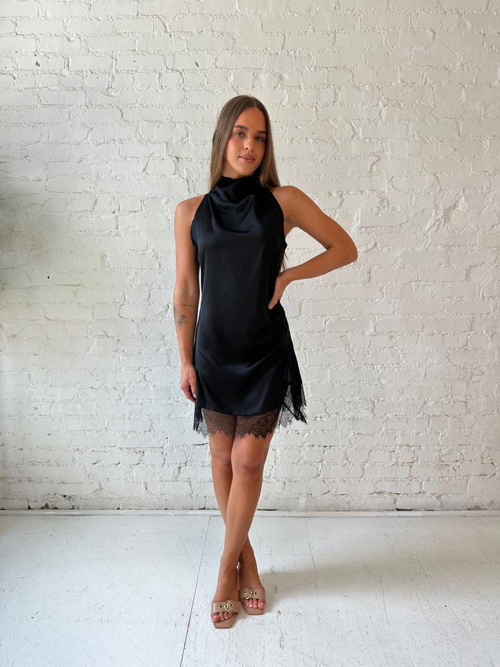 Woman wearing black satin mini dress with cowl halter neckline and lace trim detailing 
