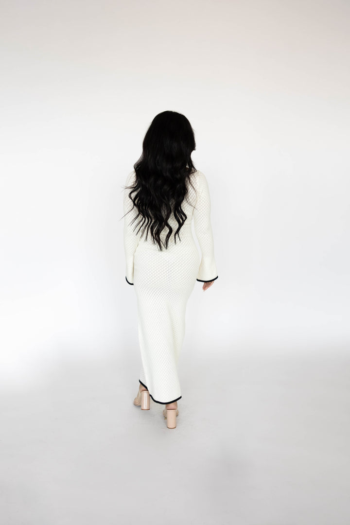 Woman wearing ivory long sleeve knit maxi dress with black contrast trim.