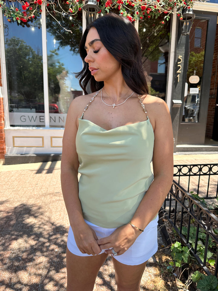 Woman wearing sage green satin halter top with beading detail, and cowl neckline. 