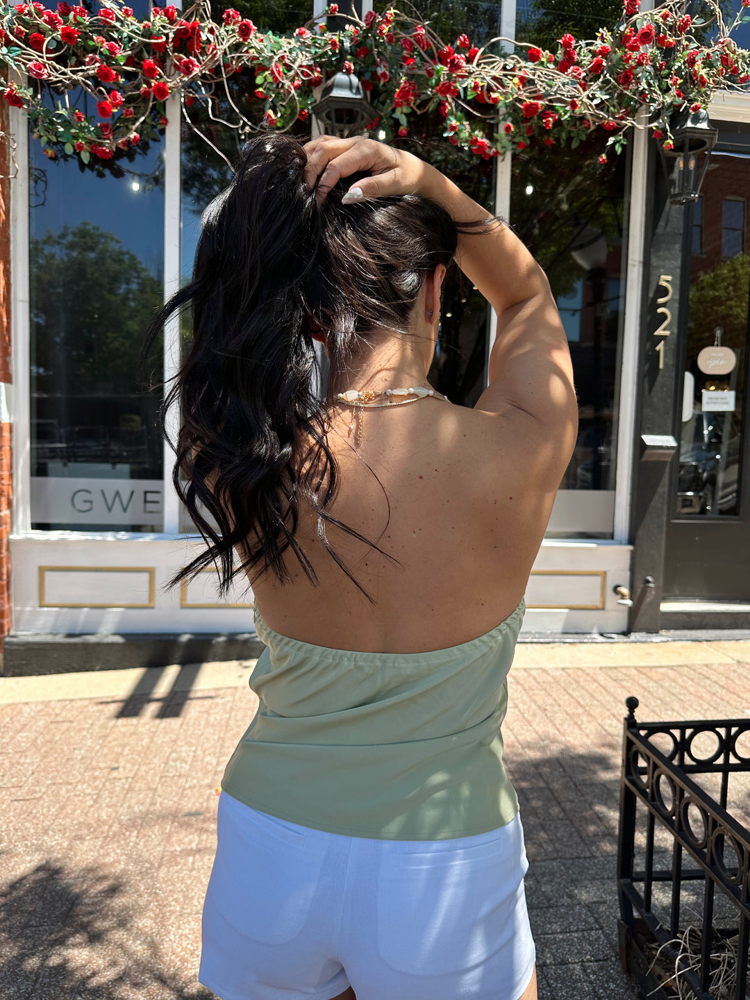 Woman wearing sage green satin halter top with beading detail, and cowl neckline. 
