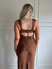 Woman wearing brown satin polka dot midi dress with cutout midsection, lace trim and tie detail.