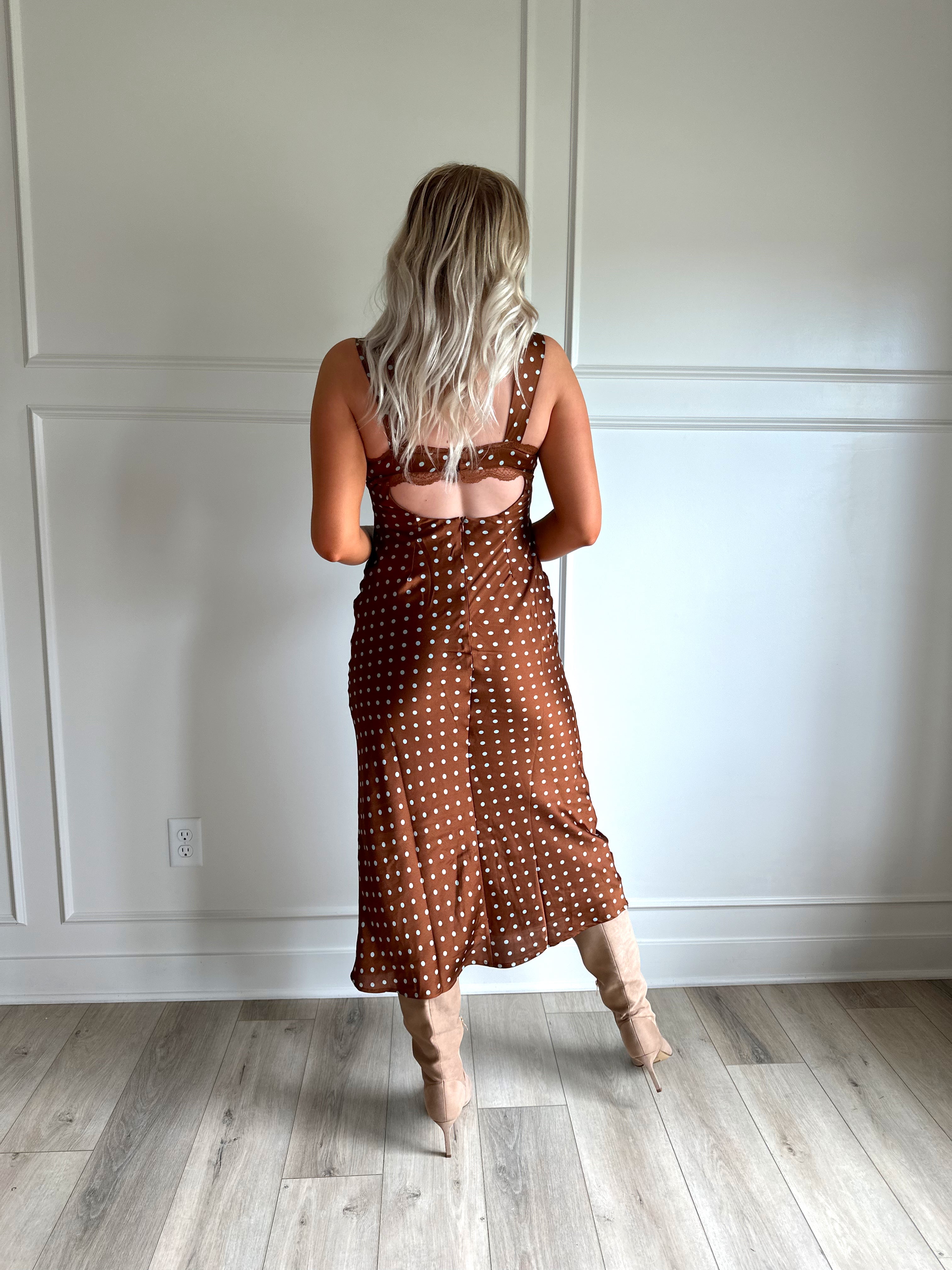 Woman wearing brown satin polka dot midi dress with cutout midsection, lace trim and tie detail.