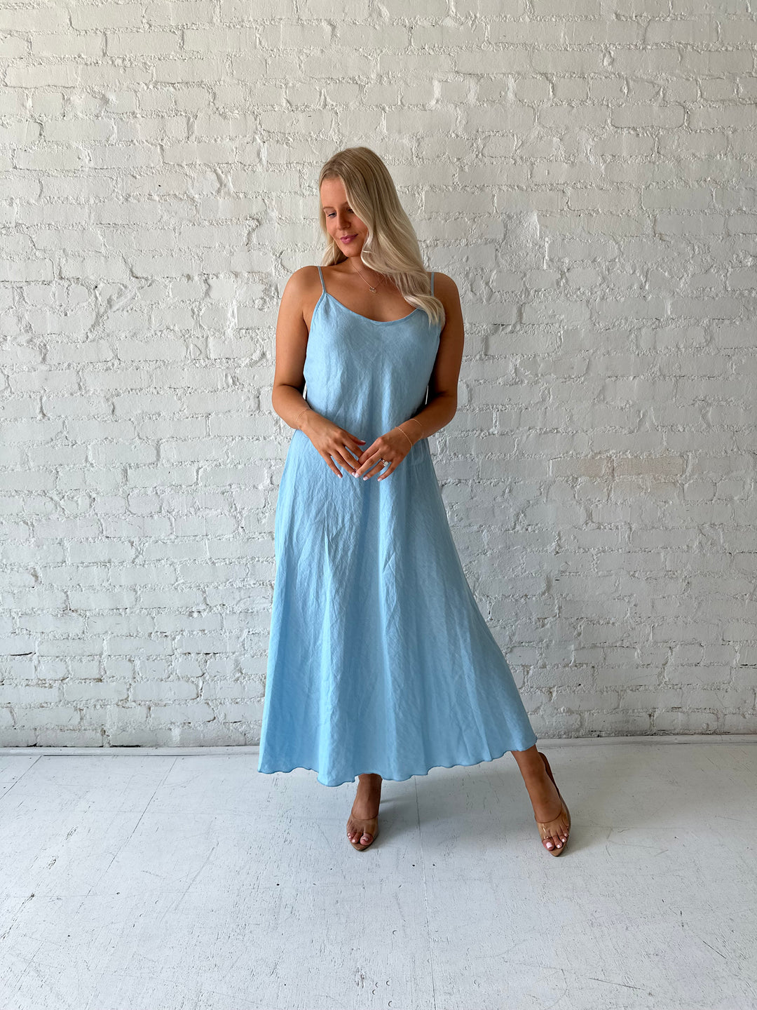 Woman wearing light blue linen slip maxi dress with adjustable spaghetti straps. 
