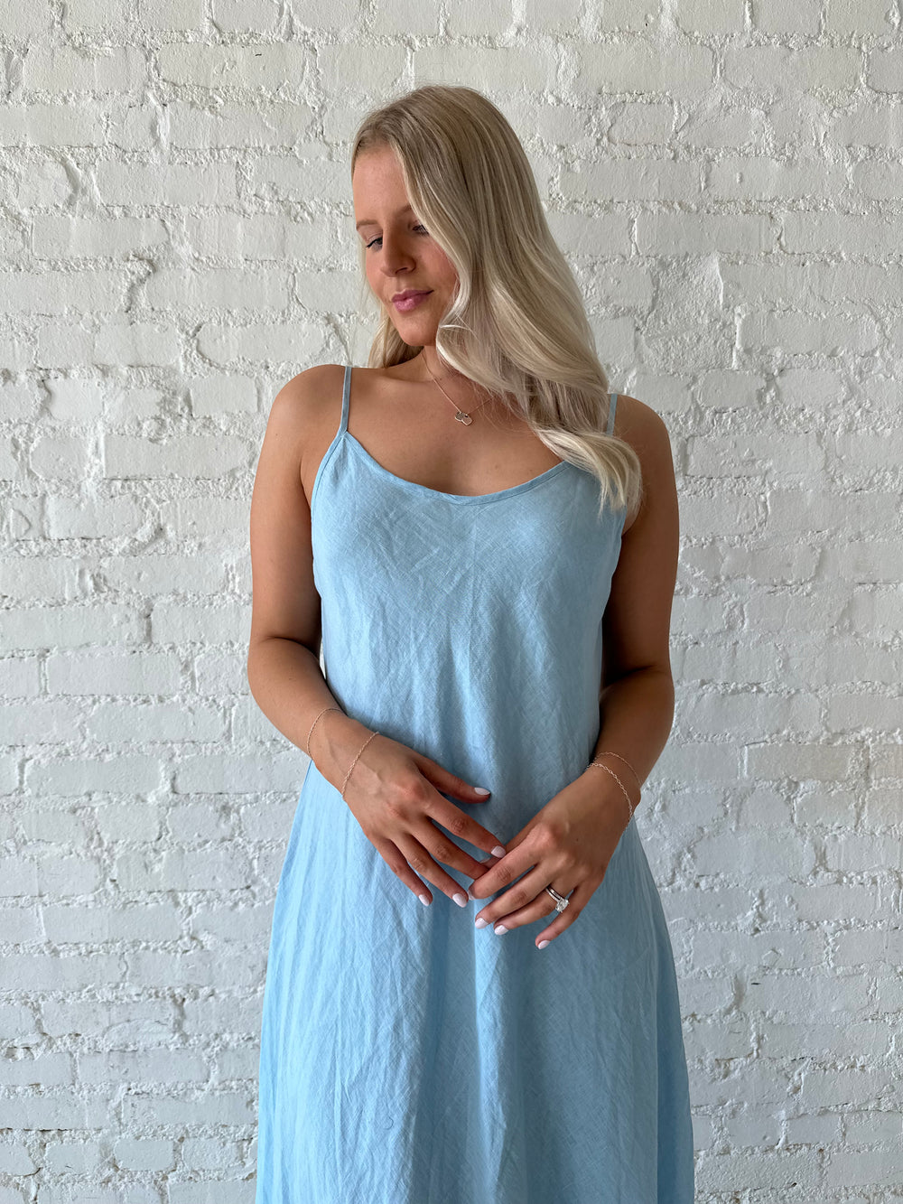 Woman wearing light blue linen slip maxi dress with adjustable spaghetti straps. 