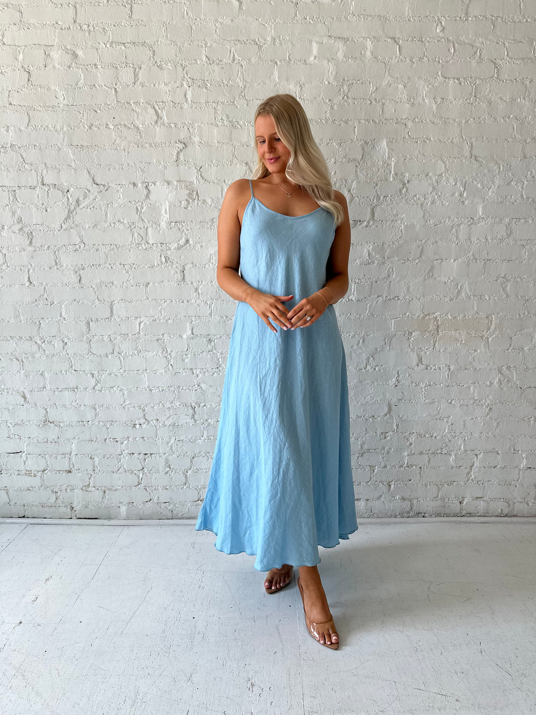 Woman wearing light blue linen slip maxi dress with adjustable spaghetti straps. 