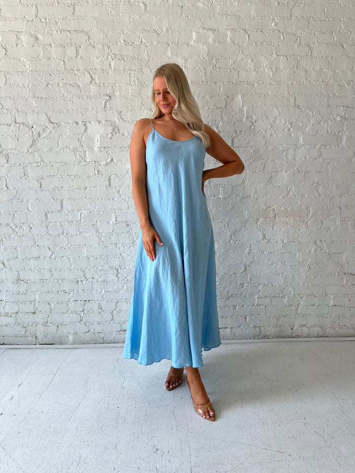 Woman wearing light blue linen slip maxi dress with adjustable spaghetti straps. 