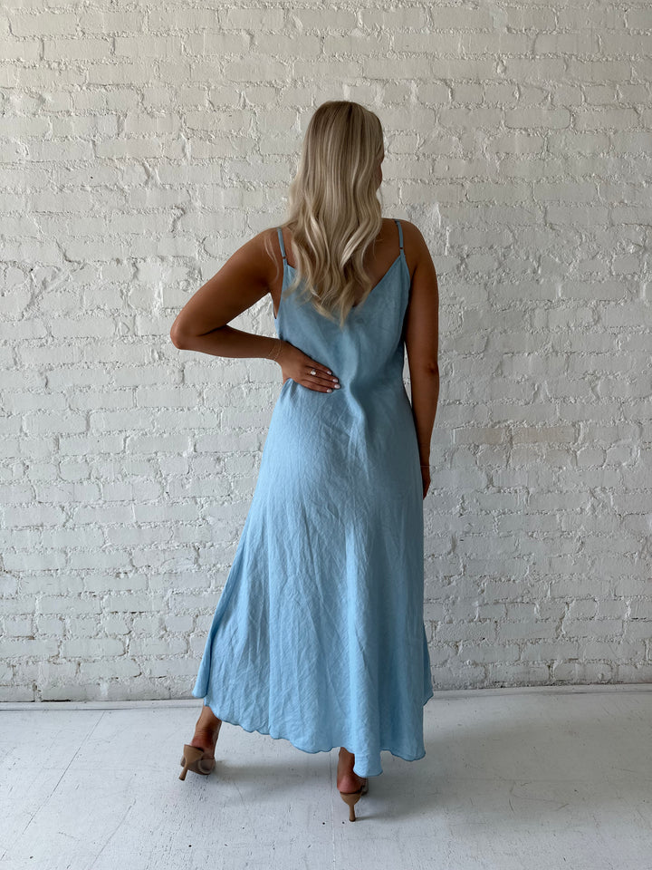 Woman wearing light blue linen slip maxi dress with adjustable spaghetti straps. 