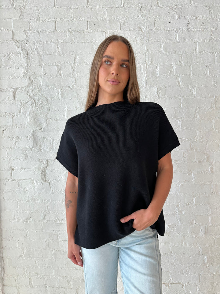 Woman wearing an oversized black knit short sleeve sweater top with light wash barrel jean. 