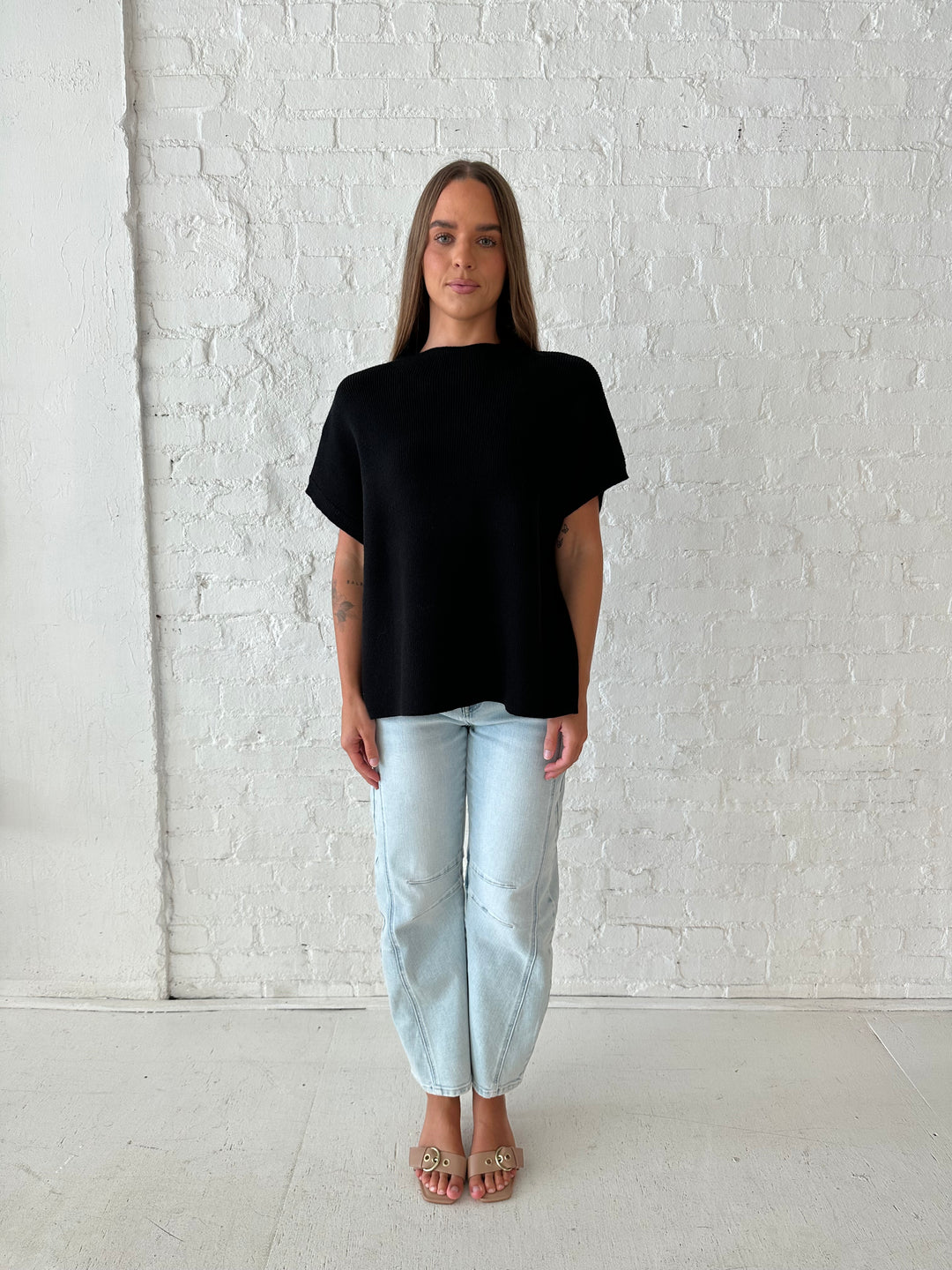 Woman wearing an oversized black knit short sleeve sweater top with light wash barrel jean. 