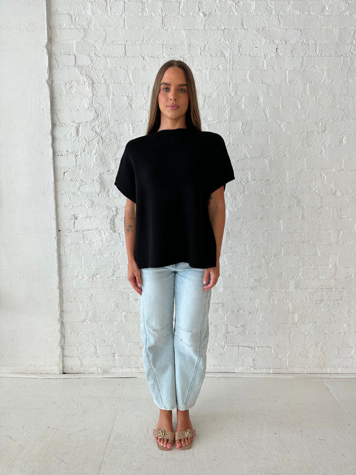 Woman wearing an oversized black knit short sleeve sweater top with light wash barrel jean. 
