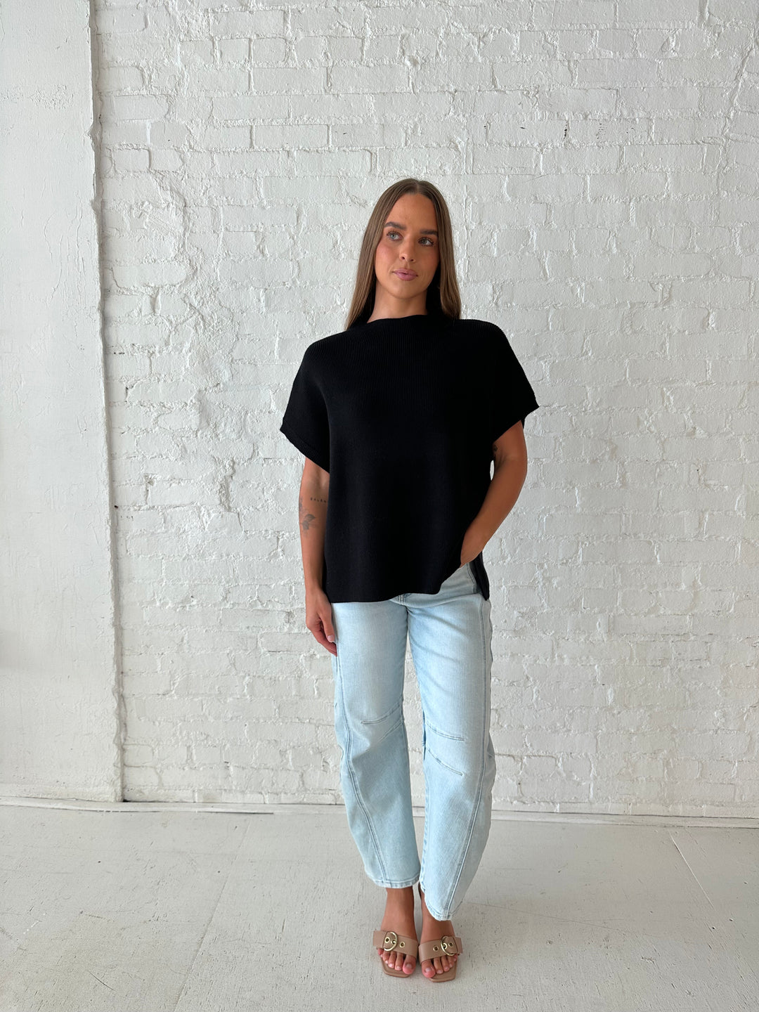 Woman wearing an oversized black knit short sleeve sweater top with light wash barrel jean. 