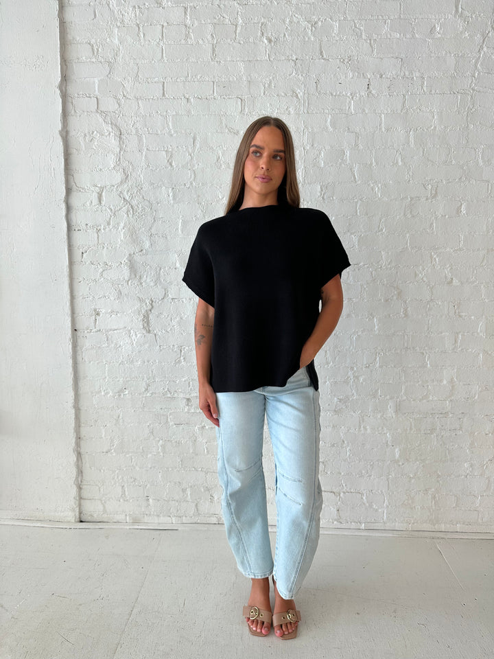 Woman wearing an oversized black knit short sleeve sweater top with light wash barrel jean. 