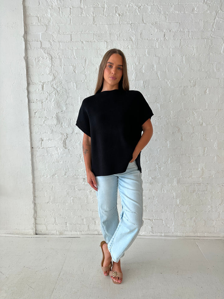 Woman wearing an oversized black knit short sleeve sweater top with light wash barrel jean. 