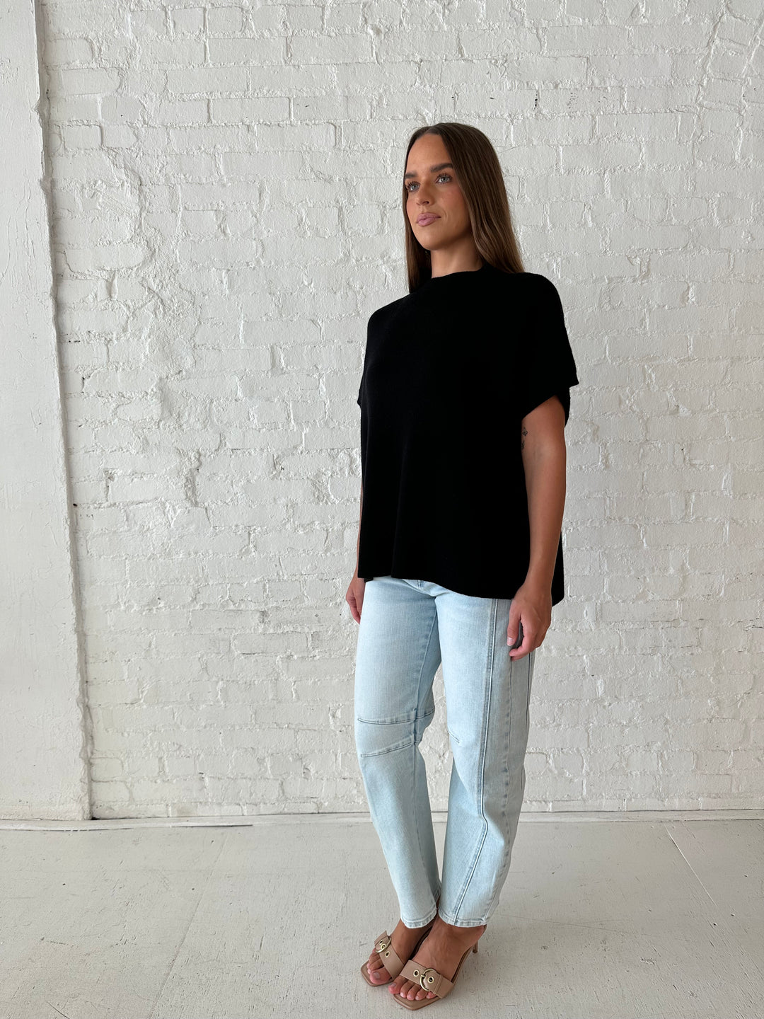 Woman wearing an oversized black knit short sleeve sweater top with light wash barrel jean. 