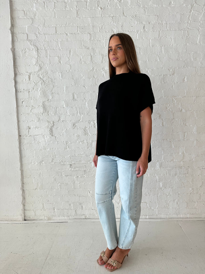 Woman wearing an oversized black knit short sleeve sweater top with light wash barrel jean. 