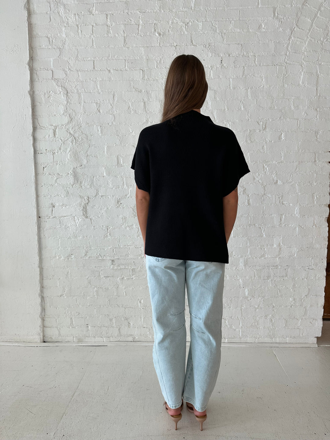 Woman wearing an oversized black knit short sleeve sweater top with light wash barrel jean. 