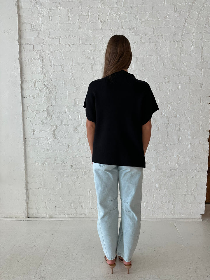 Woman wearing an oversized black knit short sleeve sweater top with light wash barrel jean. 