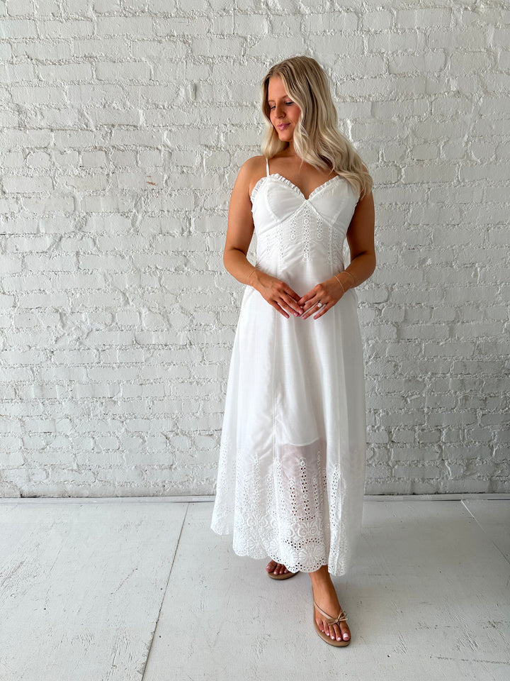 Woman wearing white eyelet maxi dress with open back, and functional pockets. 