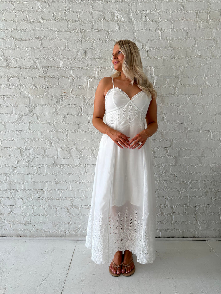 Woman wearing white eyelet maxi dress with open back, and functional pockets. 