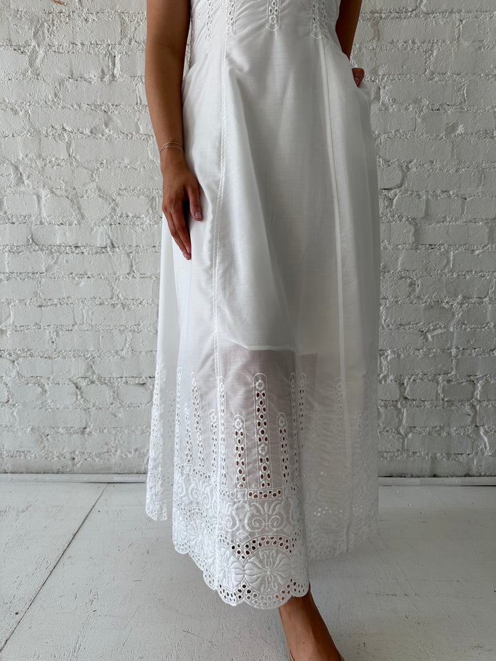 Woman wearing white eyelet maxi dress with open back, and functional pockets. 