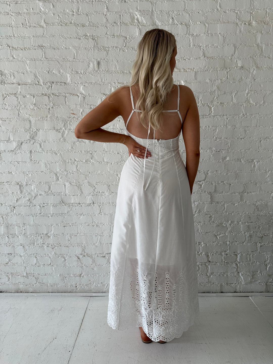 Woman wearing white eyelet maxi dress with open back, and functional pockets. 