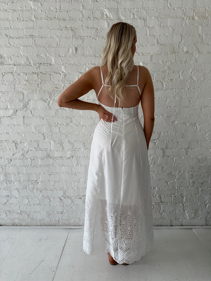 Woman wearing white eyelet maxi dress with open back, and functional pockets. 