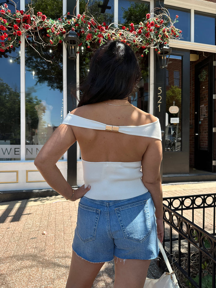 Woman wearing off white knit off the shoulder top with open back and metal detail.