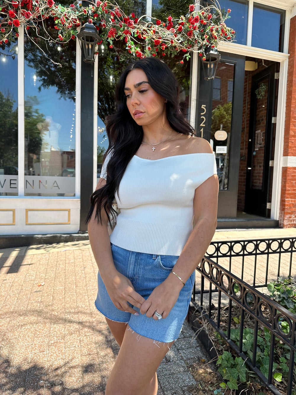 Woman wearing off white knit off the shoulder top with open back and metal detail.