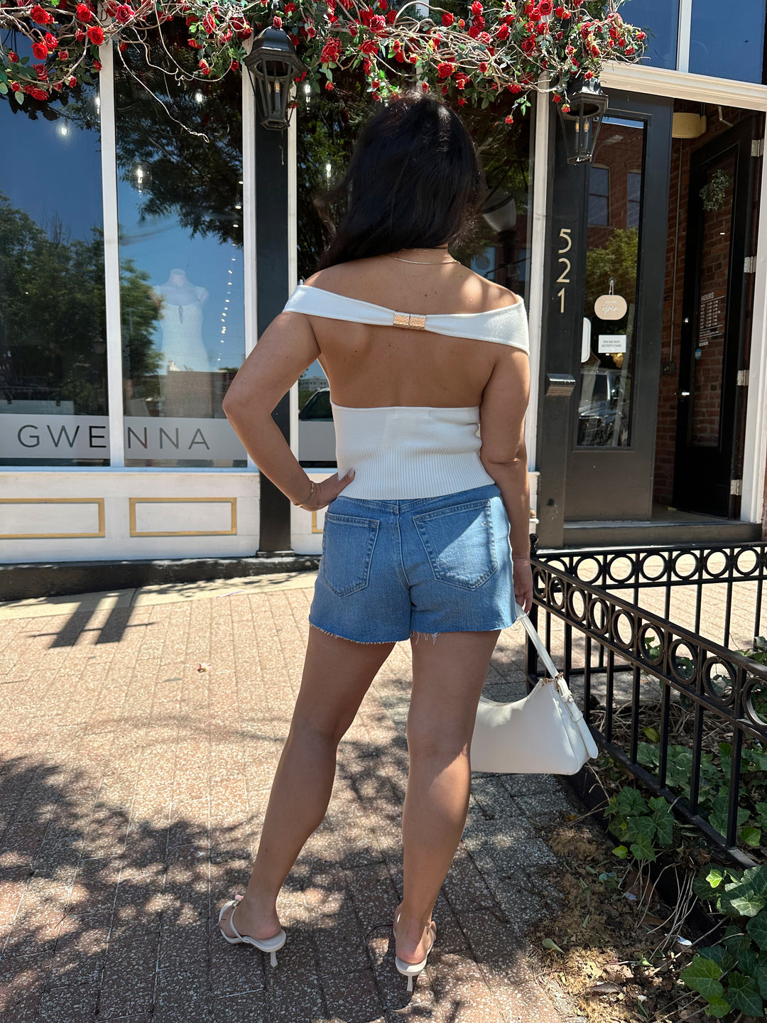 Woman wearing off white knit off the shoulder top with open back and metal detail.