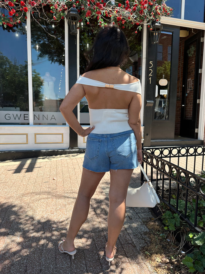 Woman wearing off white knit off the shoulder top with open back and metal detail.