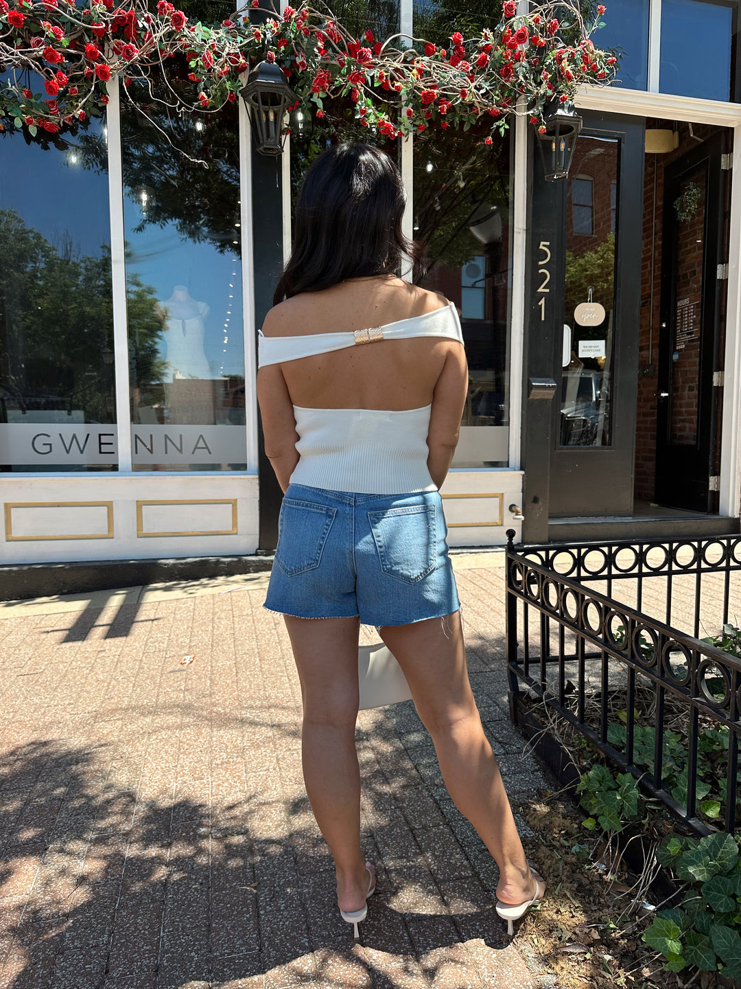 Woman wearing off white knit off the shoulder top with open back and metal detail.