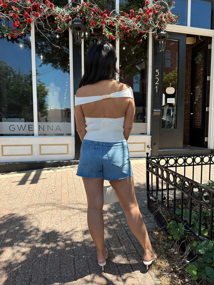 Woman wearing off white knit off the shoulder top with open back and metal detail.