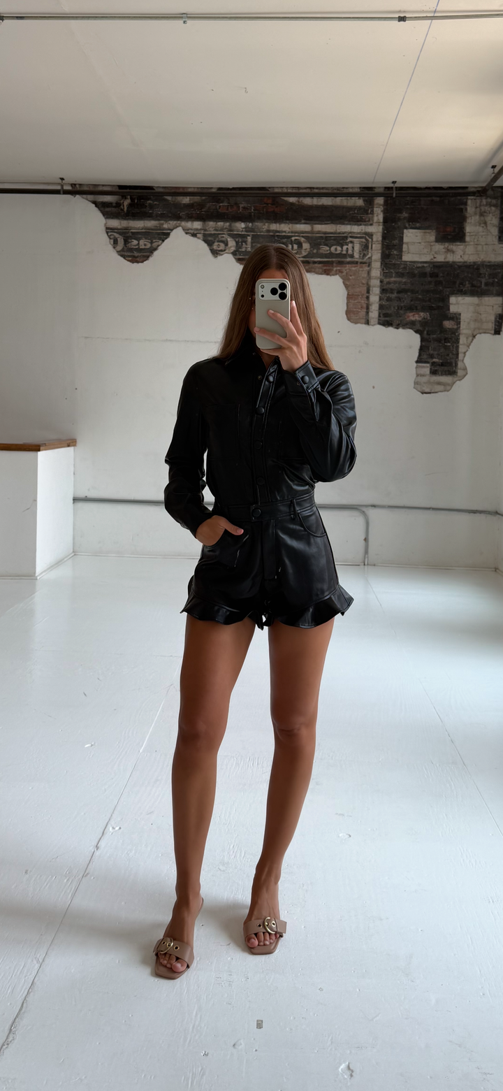 Woman wearing black leather long sleeve romper with ruffle hem.