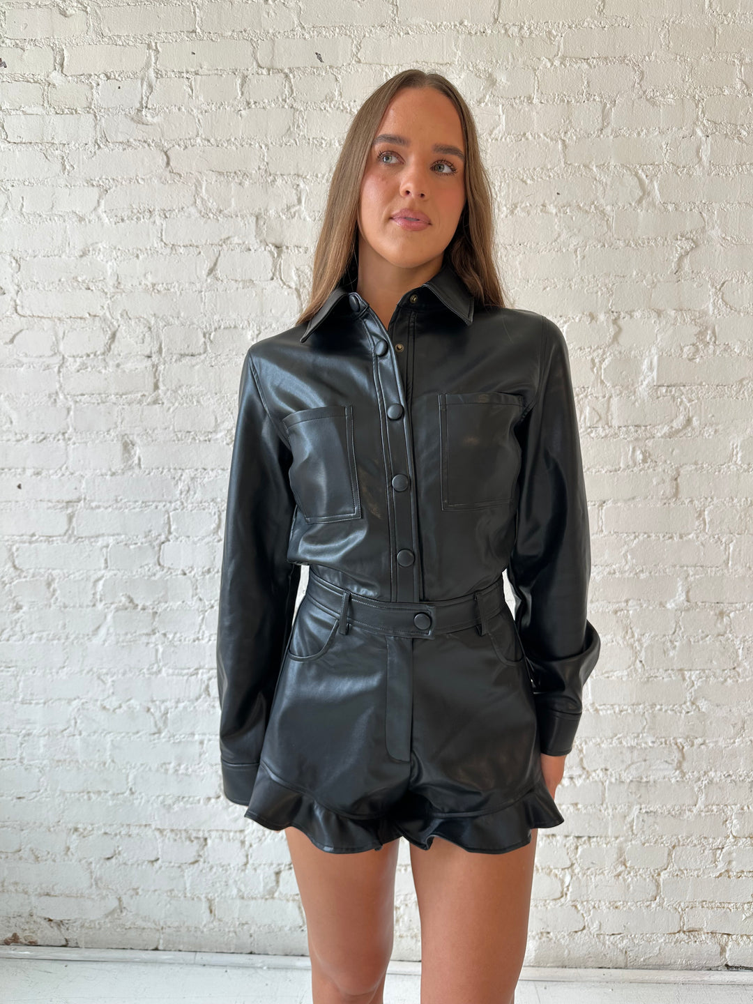 Woman wearing black leather long sleeve romper with ruffle hem.